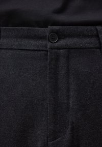 Czarne wełniane spodnie o gładkiej fakturze, z zapięciem na jeden guzik i unikalnym wzorem kieszeni, podkreślające dopasowany krój.