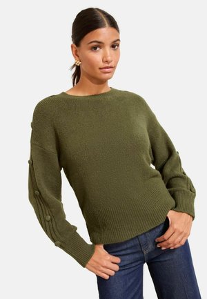 Olivgrüner, gestrickter Pullover mit geripptem Saum und Bündchen, der strukturierte Ärmel mit dekorativen Knöpfen aufweist. Kombiniert mit dunklen Jeans.