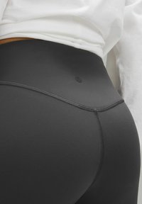 Czarne legginsy o wysokim stanie z gładką teksturą, z tonalnymi ściegami i małym logo na pasku.