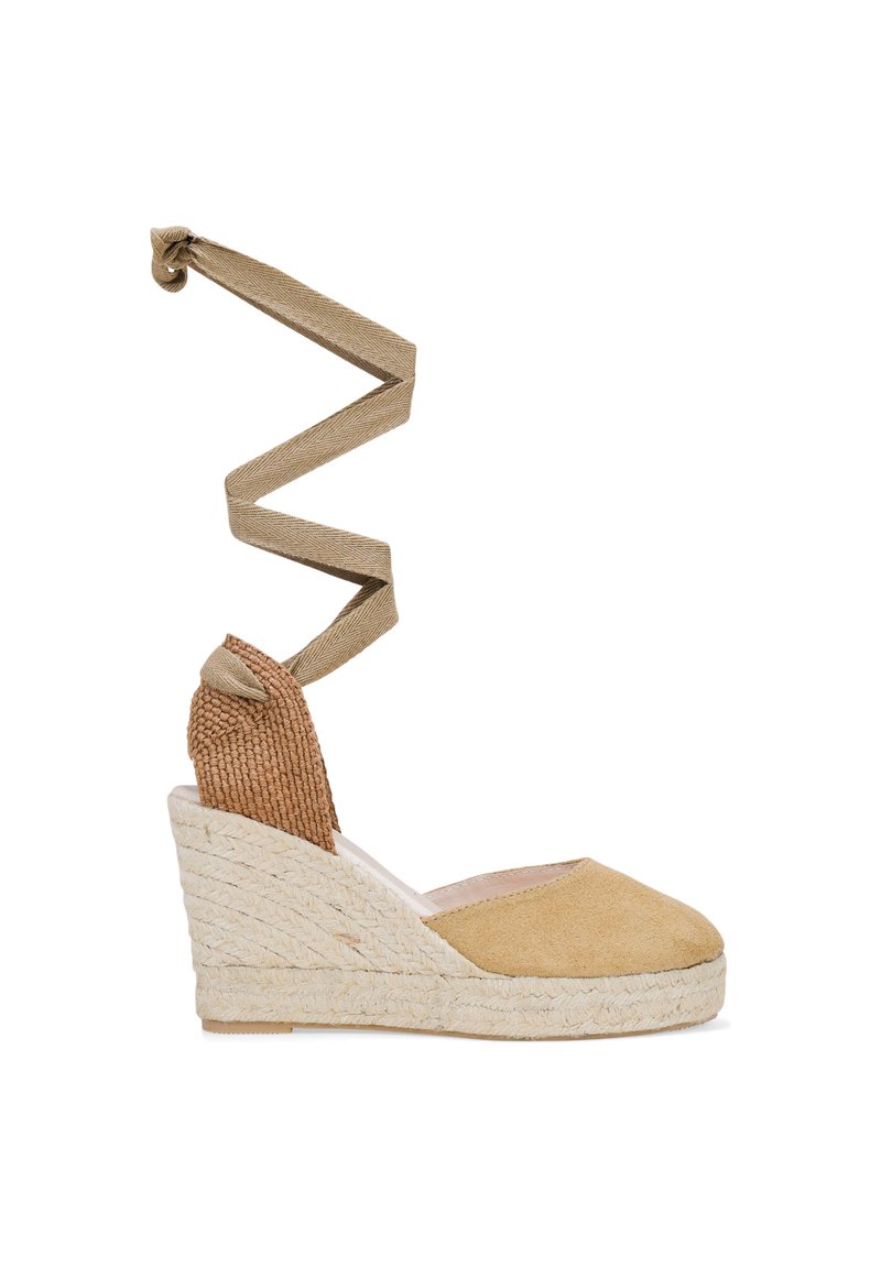 Zapato de cuña espadrille en suave ante color tostado con suela de yute trenzado y una correa de tela en espiral para el tobillo. Presenta detalles de tejido texturizado cerca del talón.