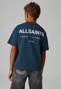 Tamsiai mėlynas medvilninis marškinėliai su dideliu baltu tekstu ant nugaros: "ALLSAINTS" ir "LONDON", po kurio yra japonų simboliai.
