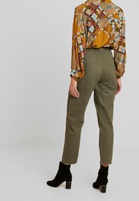 Mönstrad blus med lång ärm och geometriska mönster i brunt och gult, tillsammans med olivgröna cargobyxor och svarta klackstövlar.