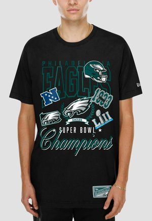 Mann trägt schwarzes Philadelphia Eagles Super Bowl Champions T-Shirt mit Logos, Footballhelm und Schrift in Grün, Weiß und Blau.