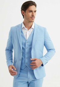 Costume trois pièces bleu clair comprenant un blazer ajusté et un gilet avec cinq boutons, associé à une chemise blanche.