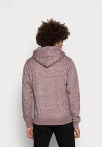 Hoodie bordeaux avec un tissu texturé, poche kangourou et capuche à cordon réglable. Présente une coupe décontractée et des poignets côtelés.