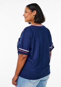 Navy blue oversized t-shirt with short sleeves. Features red and white striped accents on the collar and sleeves. Smooth fabric texture.