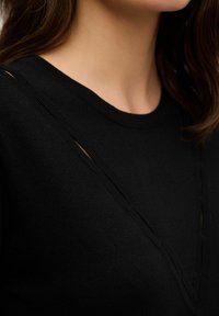 Maglione nero a maglia con scollo a V e strisce texture lungo il collo, con dettagli a taglio, che mette in evidenza una finitura in tessuto liscia.