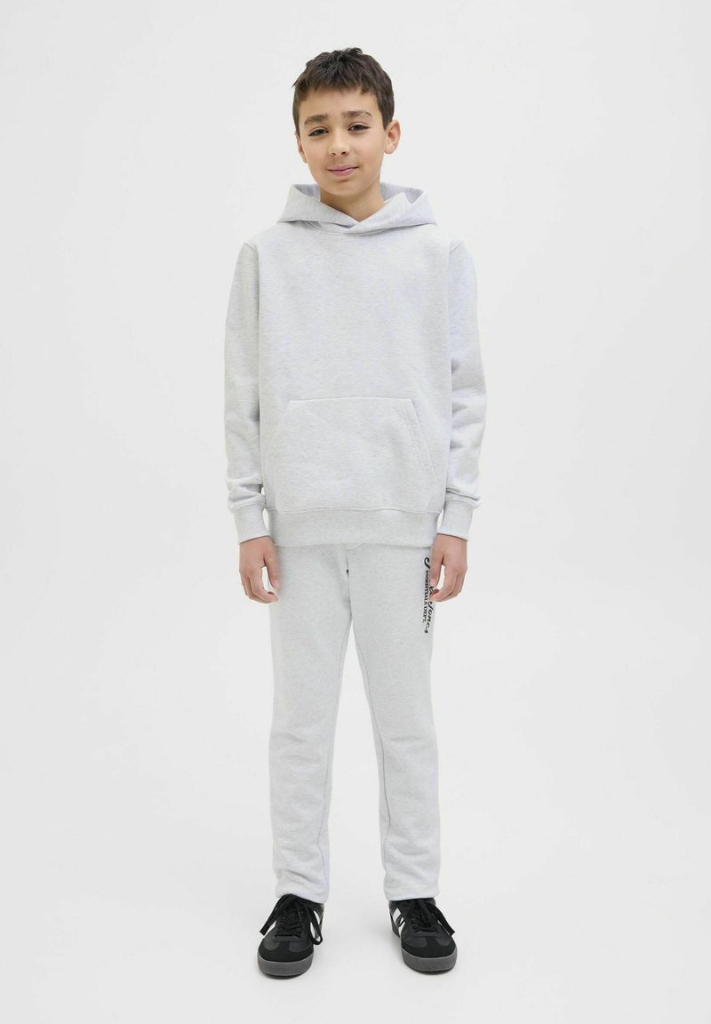 Grauer Hoodie mit Kängurutasche, kombiniert mit grauen Jogginghosen mit seitlichem Logo-Detail. Tragen mit schwarzen Sportschuhen. Minimalistisches Design.