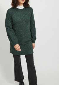 Maglione lavorato a maglia verde scuro con collo rotondo e maniche lunghe leggermente a palloncino, caratterizzato da una vestibilità rilassata e orlo a coste.
