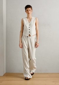 Ensemble en deux pièces comprenant un gilet sans manches à boutons et un pantalon rayé taille haute, ample, en tissu léger avec une finition texturée.