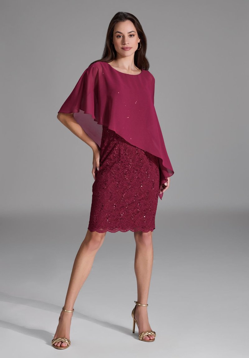Robe bordeaux avec une cape en chiffon superposée et des détails en dentelle, présentant un ourlet ondulé et des embellissements subtils. Des sandales à talons hauts complètent le look.