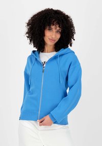 Blauwe zip-up hoodie met een capuchon met trekkoord, zachte textuur, ribbelboorden en -zoom. Draag met een wit graphic t-shirt eronder.