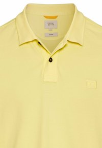 Gelbes Polohemd aus biologischem Stoff. Mit einer Knopfleiste mit zwei Knöpfen, kurzen Ärmeln und einem gestickten Logo auf der Brust.