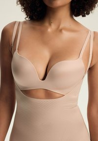Biustonosz w kolorze nude z dekoltem w szpic, formowanymi miseczkami i cienkimi regulowanymi ramiączkami. Posiada wycięcie poniżej biustu z subtelną teksturą.