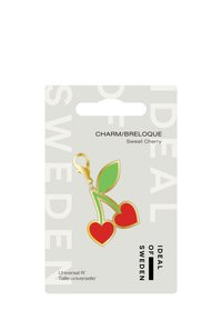 Charm di ciliegia rossa con foglie verdi, dotato di una clip in metallo dorato per il fissaggio. Imballato su uno sfondo grigio chiaro con testo nero.