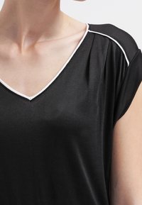 Černý krátký rukáv top s výstřihem do V a bílým akcentem. Hladká textura a volný střih zdůrazňují ležérní design.