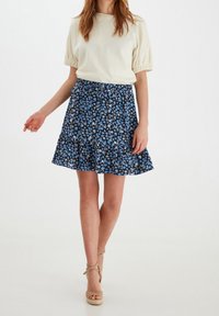 Falda floral azul con dobladillo acampanado, hecha de tela ligera. Combinada con una blusa crema con mangas abullonadas. Sandalias de cuña beige.