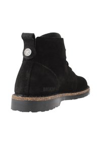 Stivaletto in suede nero, con punta rotonda, superficie testurizzata e suola in sughero. Include un loop posteriore per facilitare indossarlo e un dettaglio con il logo del marchio.