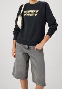 Felpa nera con logo Levi's in stampa leopardata, abbinata a pantaloni shorts in denim grigio. L'outfit è completato da una borsa a spalla di colore chiaro.