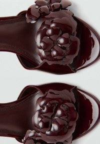 Sandales à glissière bordeaux avec un accent floral brillant sur chaque lanière ; texture lisse et brillante ; design à bout ouvert.