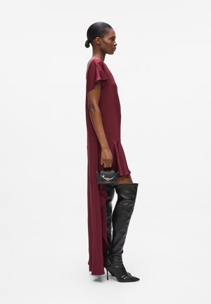 Burgundy dress with flutter sleeves, fitted bodice, and asymmetric hem. Paired with black thigh-high boots and a small handbag.