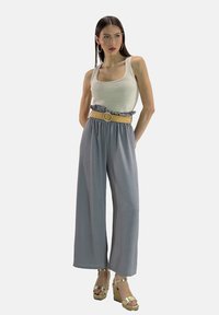 Pantalons larges gris clair avec une taille froncée, associés à un débardeur blanc et une ceinture beige tissée. Des sandales compensées dorées complètent le look.