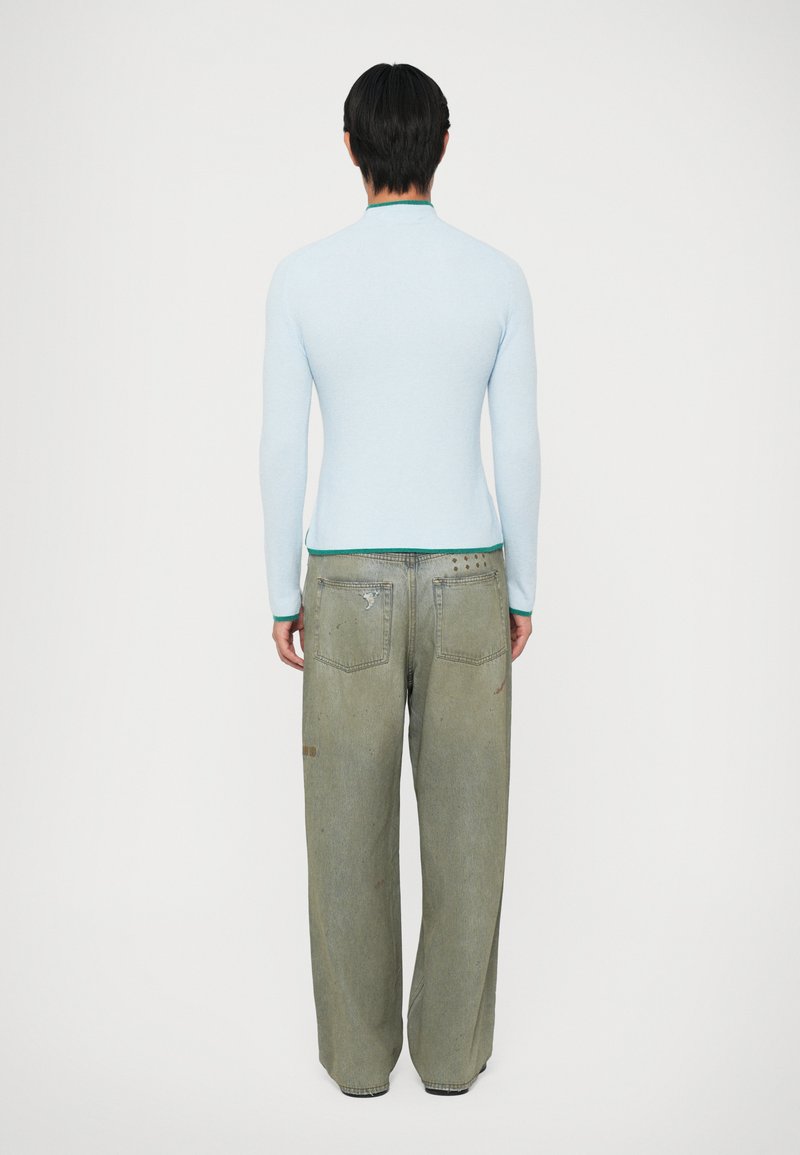 Ljusblå långärmad skjorta med en figurnära design och grön accent vid kragen, kombinerad med överdimensionerade ljusgröna jeans med slitningar.