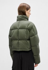 Veste courte en duvet verte avec un col haut, un design matelassé et une texture lisse et brillante. Vue arrière avec des panneaux cousus et sans fermetures.