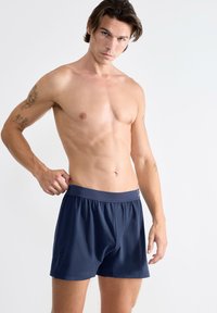 Boxers bleu marine en tissu lisse, dotés d'une taille élastique et d'un détail de logo sur les côtés. Longueur courte avec une coupe décontractée.