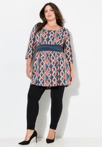 Tunic multicolore con motivo, maniche a 3/4, una cintura scura in vita, abbinata a leggings neri e tacchi alti. Tessuto morbido.