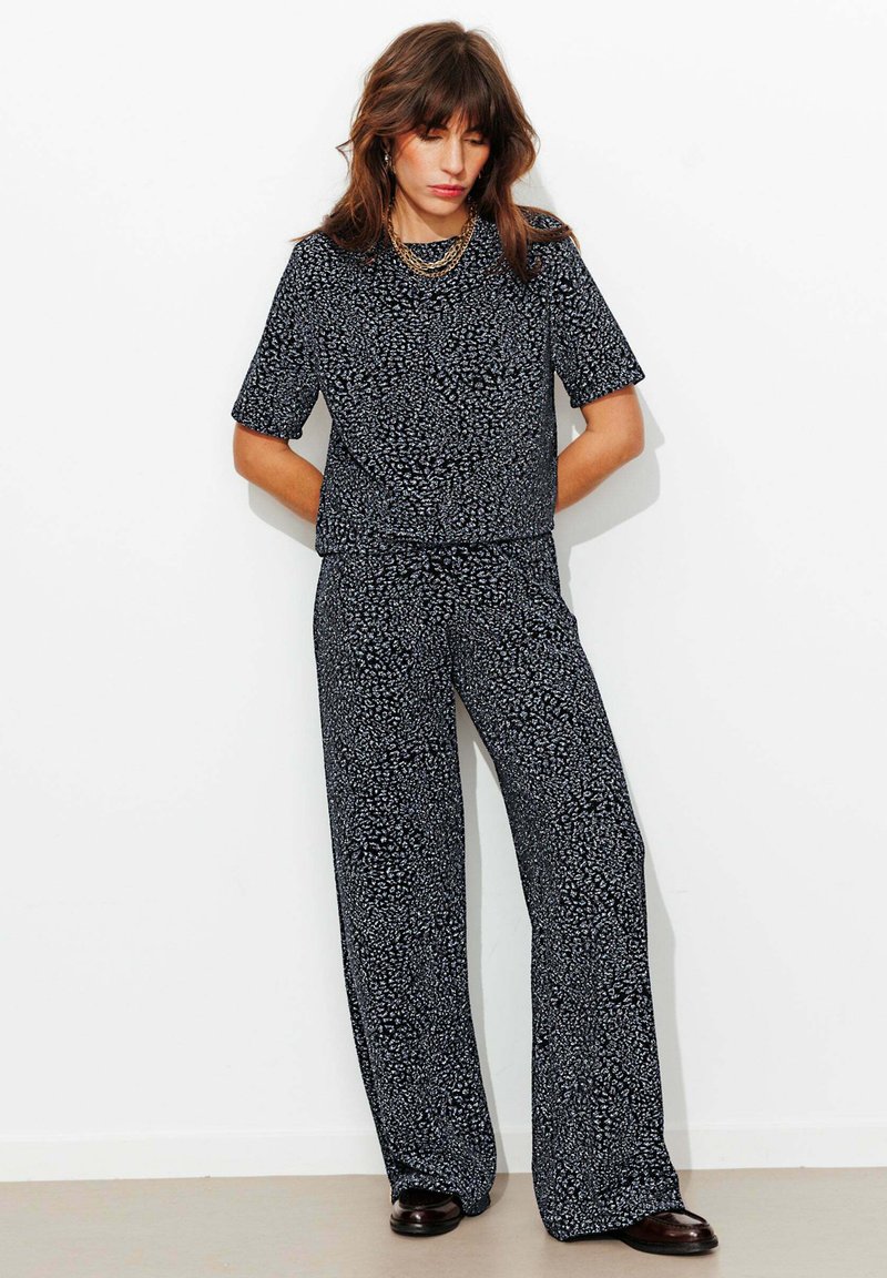 Ensemble deux pièces composé d'un haut à manches courtes et d'un pantalon à jambes larges, en tissu noir avec un petit motif blanc.