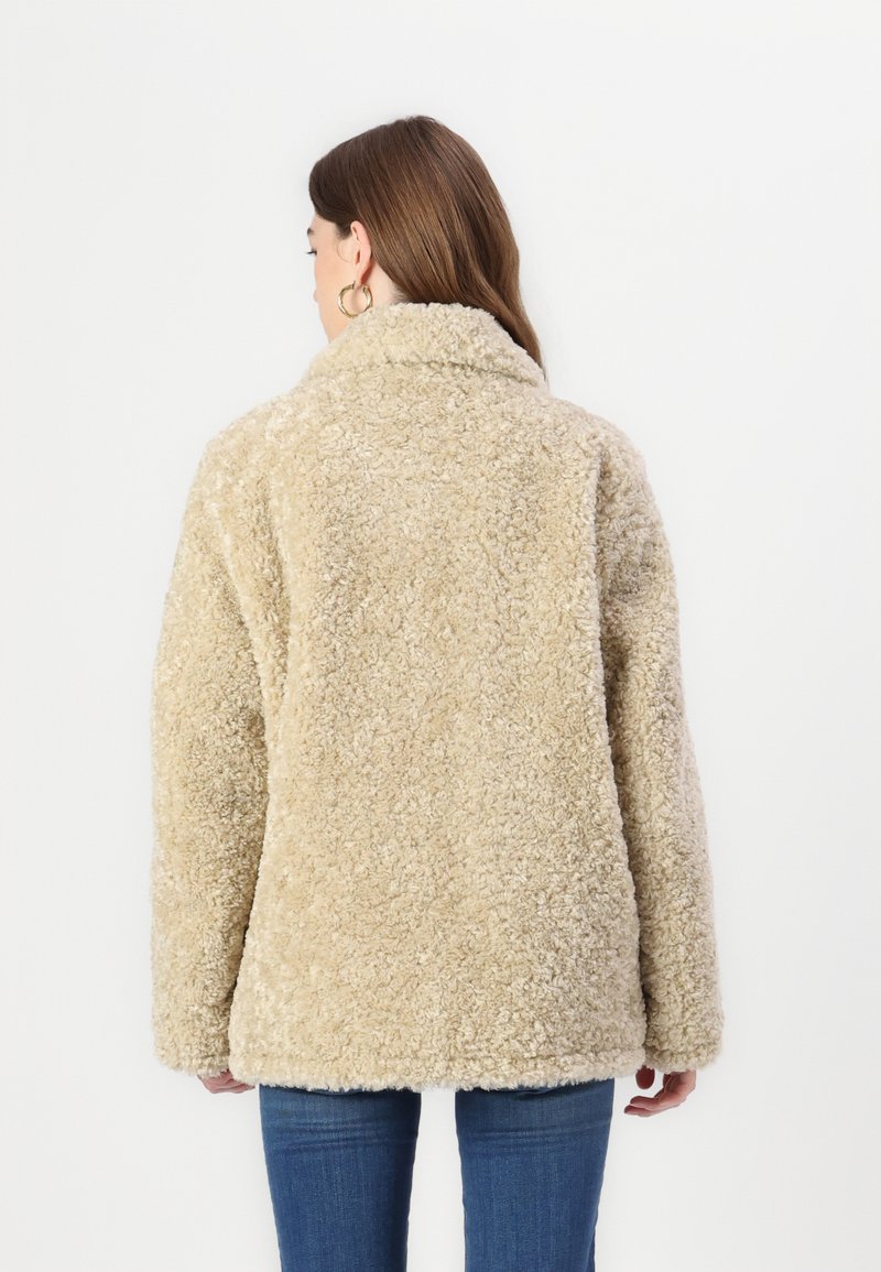 Vezelige beige schapenvachtjas met een omgevouwen kraag en lange mouwen, met een relaxed fit en een zachte, textuurachtige oppervlakte.