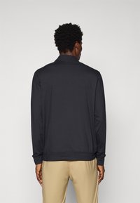 Čierny polo s dlhým rukávom a stojatým golierom, vyrobený z hladkého materiálu, so priliehavým strihom a rebrovanými manžetami a spodným lemom.