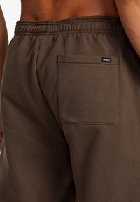 Braune Sweatpants mit einem elastischen Bund und einer einzelnen Gesäßtasche. Hergestellt aus weichem Stoff mit einem minimalistischen Logoetikett auf der Tasche.