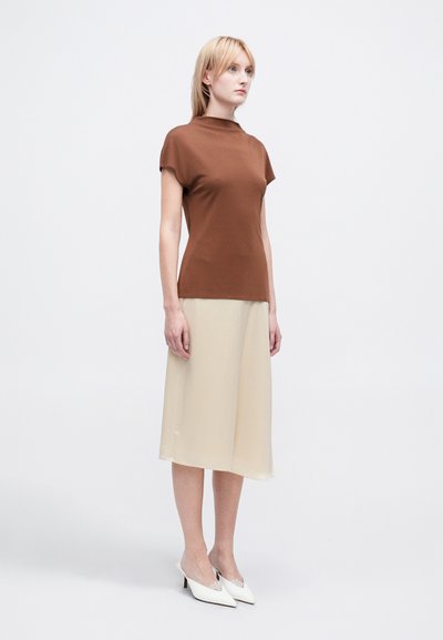 Top scurt bej din material elastic, asortat cu o fusta midi fluidă bej. Purta pantofi cu toc ascuțit albi.