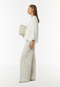 Übergroßer gestrickter Pullover in Off-White, kombiniert mit weitem Hosen in hellbeige. Hält eine gepolsterte beigen Tasche mit einem Riemen.