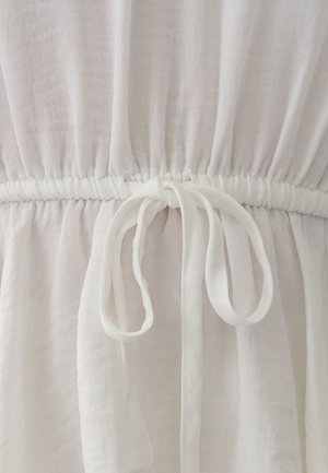 Balta auduma kleita ar savilktu jostu, centrā ar sasietu loku, uzsverot mīksta, teksturēta auduma izskatu.