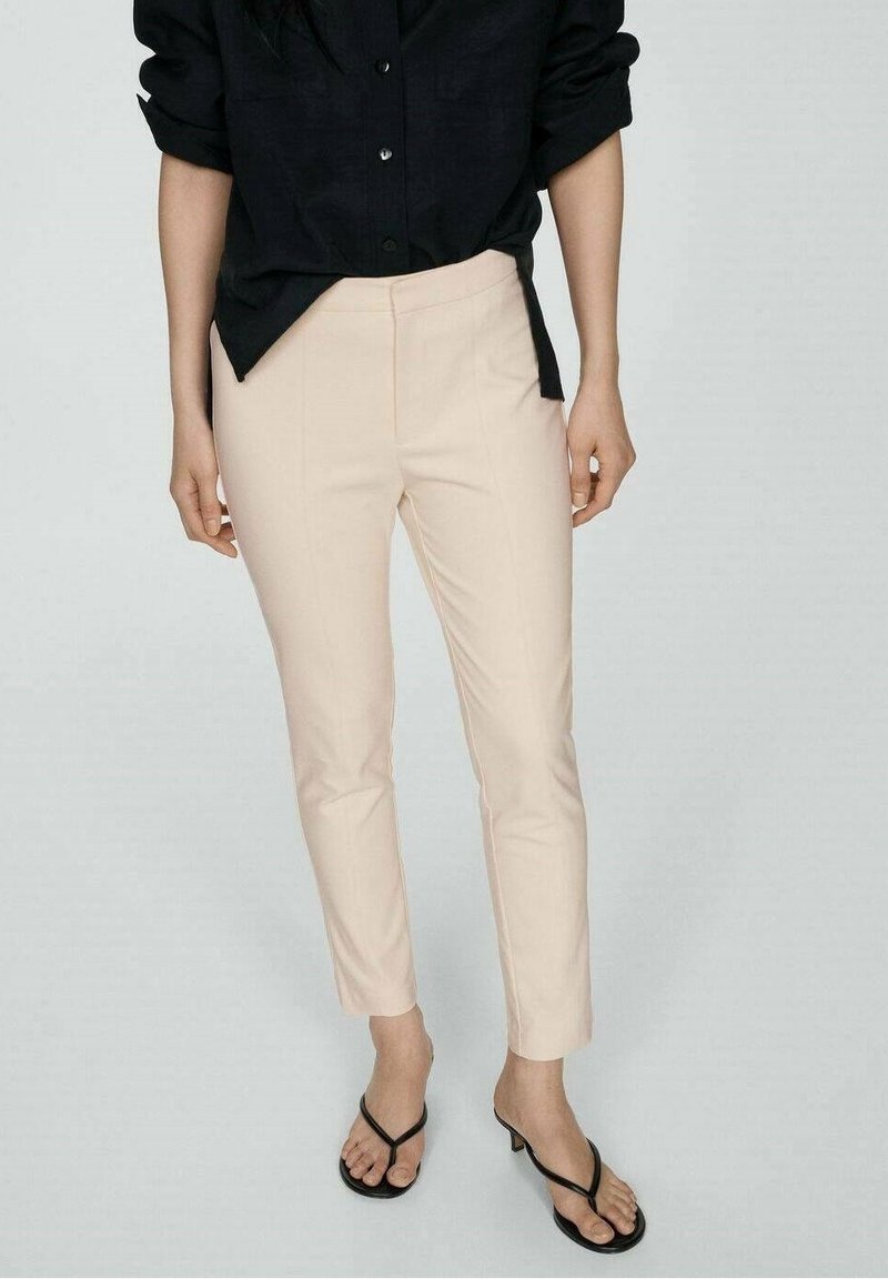 Pantalons ajustés rose clair avec une coupe slim et longueur cheville, associés à une chemise noire à boutons. Texture lisse, détails minimaux.