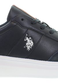 Marinblå lädersneakers med vit sula, som har snören och en silvrig polo-logotyp. Slät textur med rundad tå och kontrasterande sömmar.