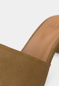 Καφέ σουέντ πέδιλο με ψηλό τακούνι, λείο δερμάτινο πάτο, ανοιχτή μύτη και μινιμαλιστικό σχέδιο. Διαθέτει κομψό σχήμα και απαλή υφή.