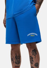 Shorts en coton bleu, avec une coupe décontractée, ornés de broderies "GOODFORNOTHING" et de détails de couture subtils.