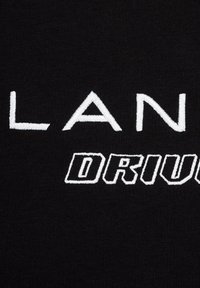 Czarna tkanina z białym haftowanym tekstem "PLAN DRIV" w wyraźnej, nowoczesnej czcionce. Gładka faktura, zbliżenie na szczegóły szycia.