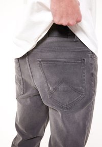 Vaqueros grises de mezclilla con un ajuste slim, con dos bolsillos traseros con detalles de costura y una etiqueta de cuero negra en la cintura.