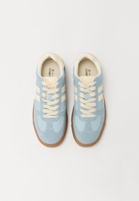 Zapatillas de ante azul claro con acentos y cordones en crema. Presentan rayas blancas y una suela de goma texturada. Diseño atlético estándar.
