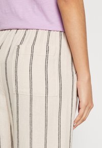 Beiga randiga byxor tillverkade av lättviktig tyg, med en avslappnad passform, elastisk midja och en liten bakficka.