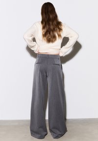 Graue Hosen mit weitem Bein und glatter Textur, versehen mit Seitentaschen und hoher Taille. Kombiniert mit einem cremefarbenen Strickoberteil.