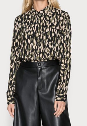 Femme portant un chemisier à manches longues à imprimé abstrait rentré dans un pantalon en cuir noir taille haute et jambes larges.