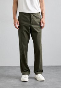 Pantalones de algodón verde oliva con corte recto, que cuentan con bolsillos laterales, cierre de botón y se llevan con zapatillas deportivas blancas.