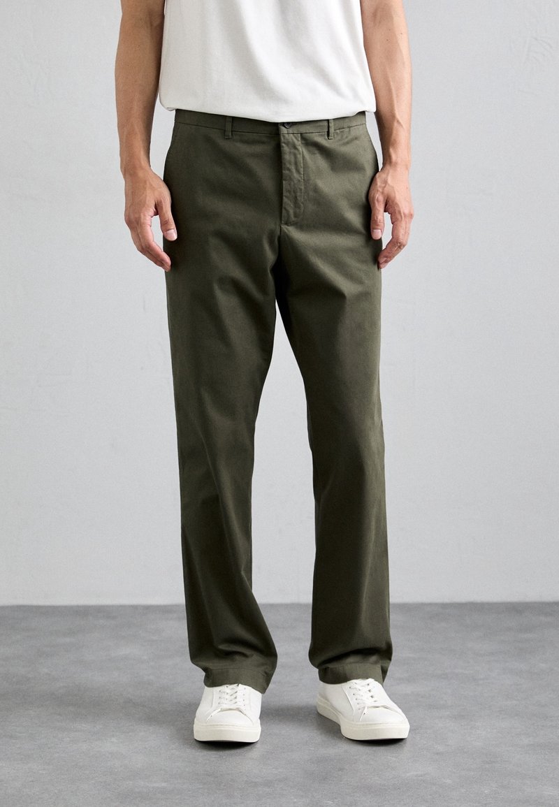 Pantalones de algodón verde oliva con corte recto, que cuentan con bolsillos laterales, cierre de botón y se llevan con zapatillas deportivas blancas.