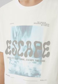 Witte katoenen t-shirt met een grafische print van water en het woord "ESCAPE" in gestileerde grijze letters, met extra tekst boven en onder.